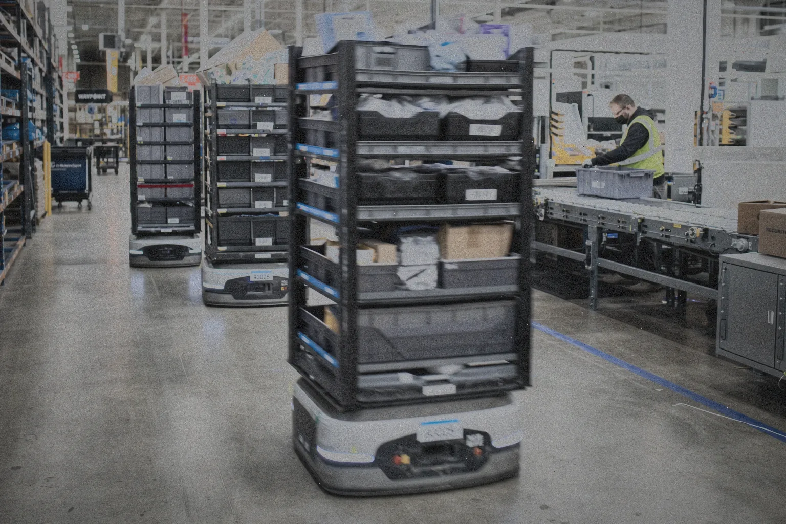 Autonomiczne roboty mobilne (AMR) przewożą regały w nowoczesnym zautomatyzowanym magazynie obok stanowiska kompletacji